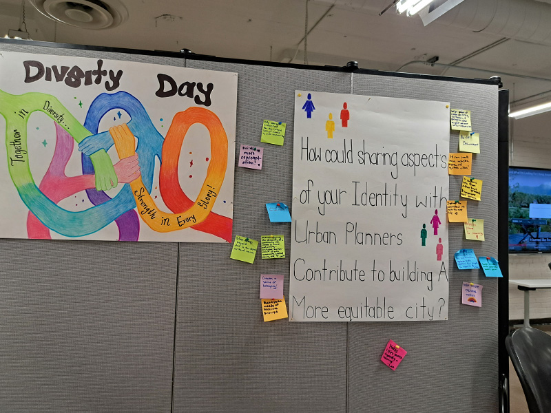 A poster with interlocking hands and the title "Diversity Day" with an sticky note activity that askes the audience "How should sharing aspects of your Identity with Urban Planners Contribute to building A More equitable city?"